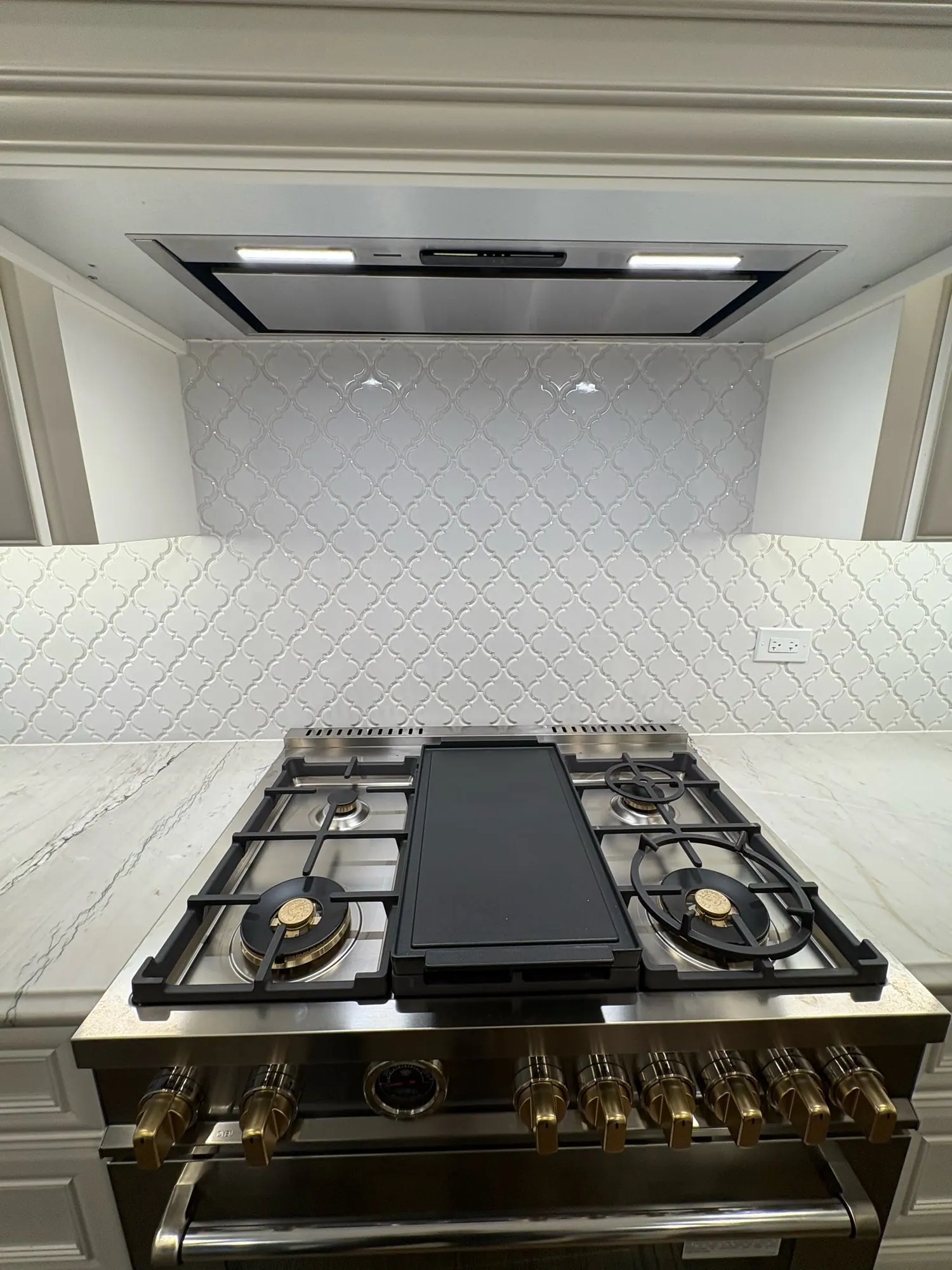 Brass range set in white shaker cabinets, with an arabesque tile backsplash and a brass pot filler.